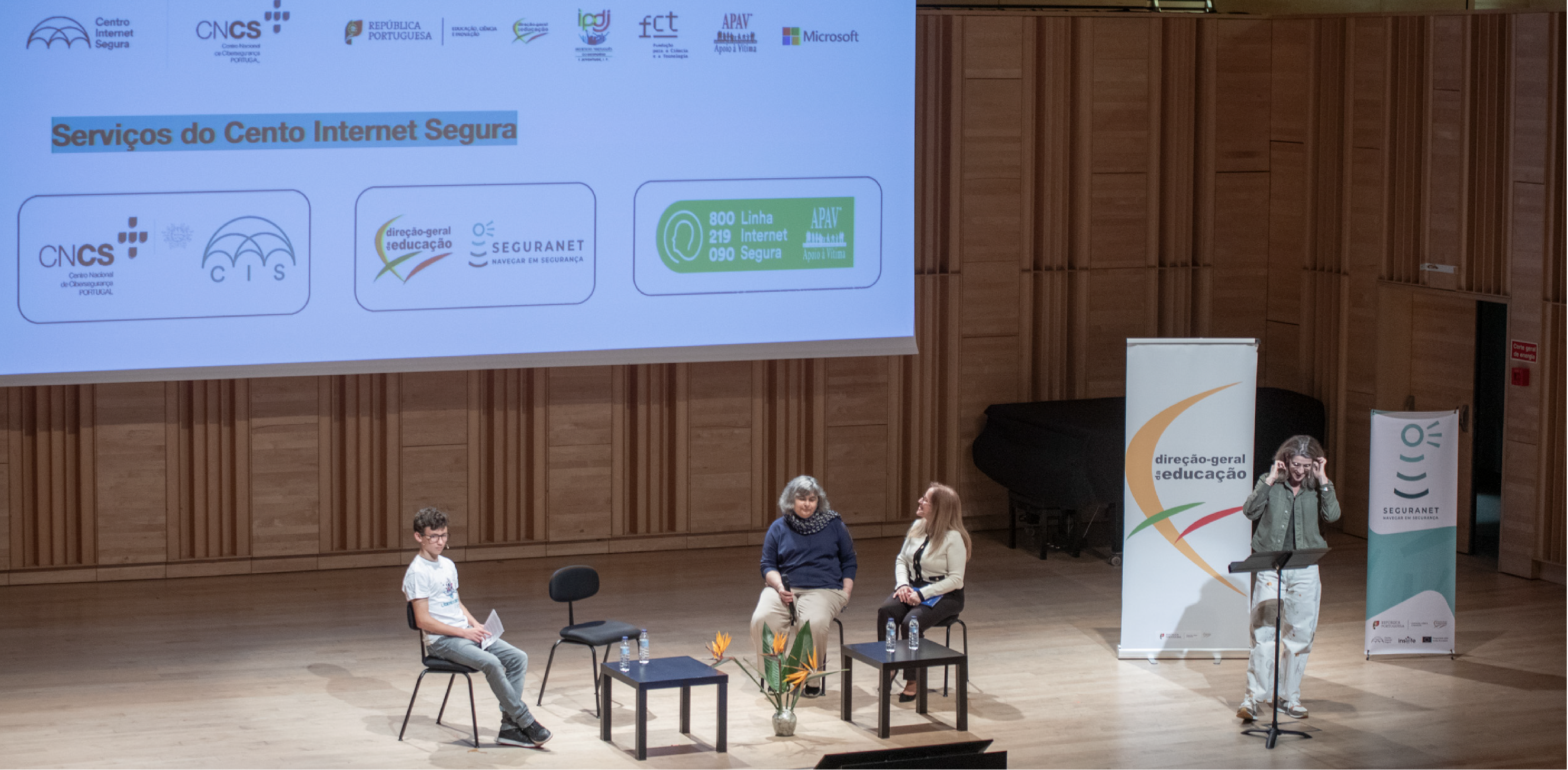 palco com três pessoas sentadas e uma mulher no púlpito como oradora. 
