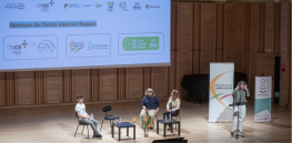 palco com três pessoas sentadas e uma mulher no púlpito como oradora. 